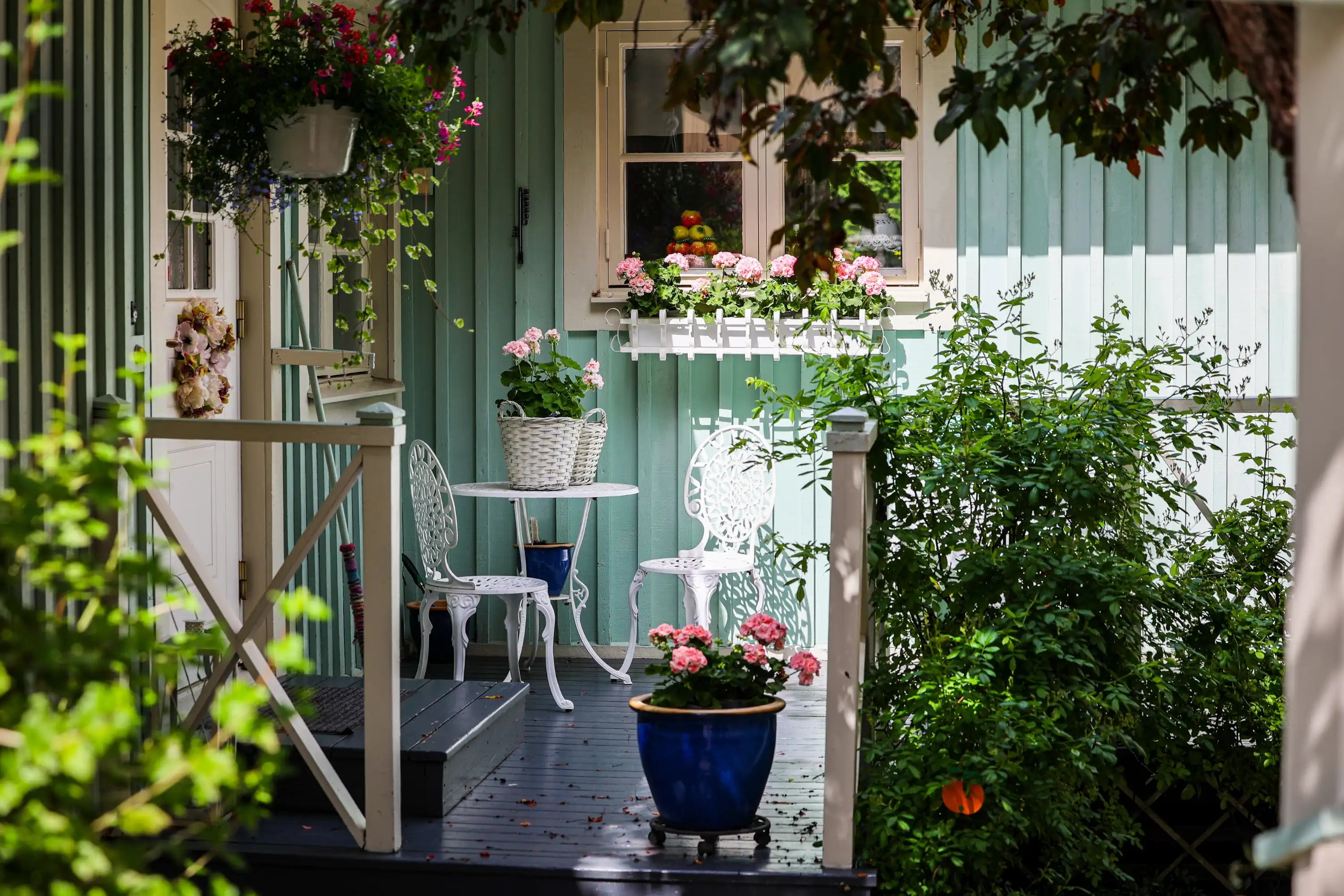 Charmante Veranda mit weißen Stühlen, einem kleinen Tisch, Topfblumen und hellgrünen Holzwänden.