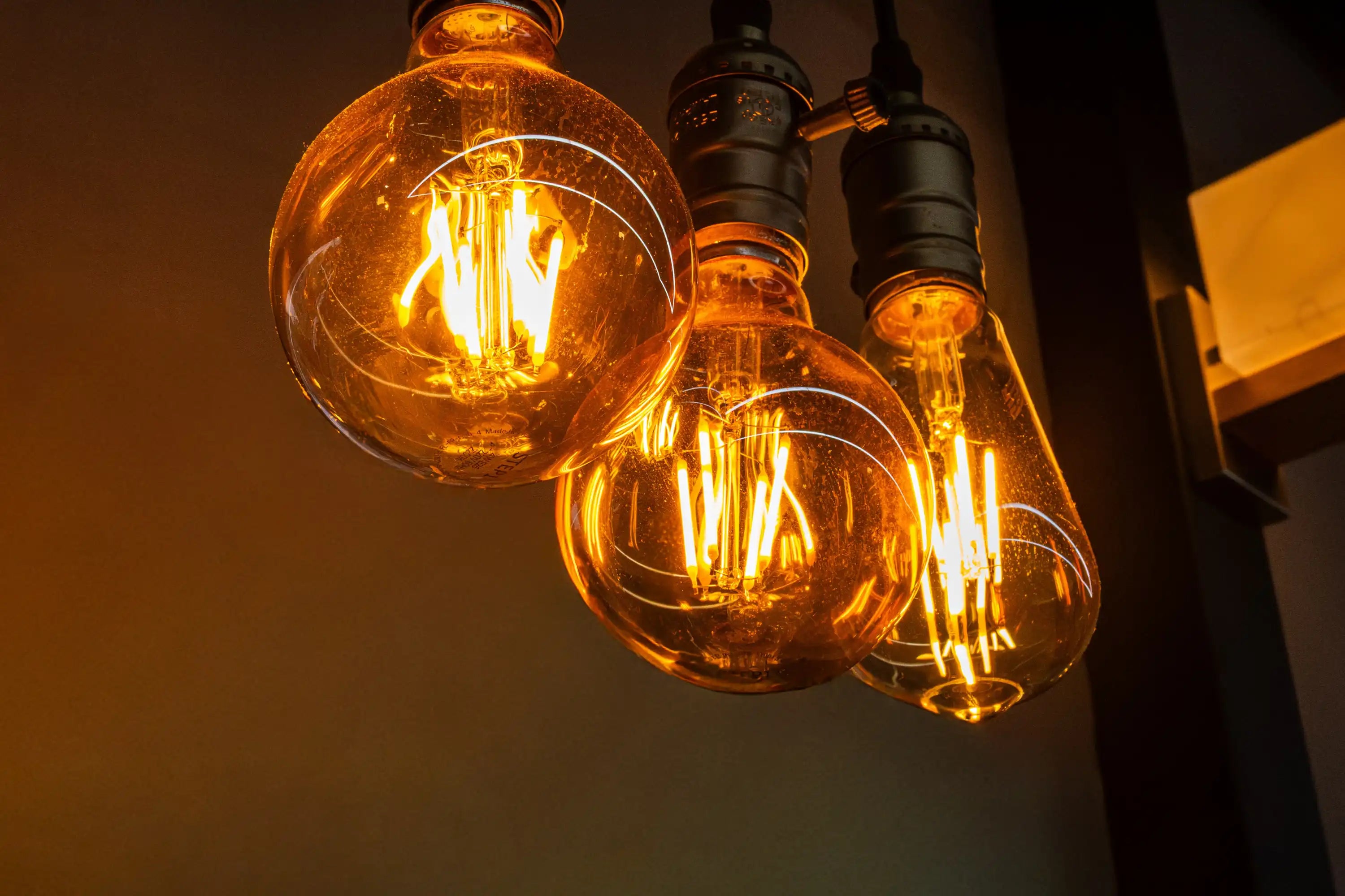Drei leuchtende Edison-Glühbirnen im Vintage-Stil hängen von der Decke vor einem dunklen Hintergrund.