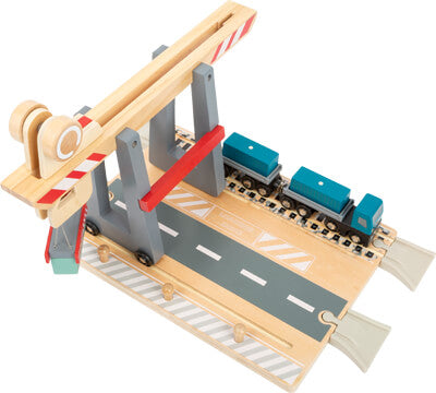 Holzspielzeug-Bahnübergang-Spielset mit einer Straße, Schranken und einer blauen Spielzeugeisenbahn auf Schienen. Die Funktionen können mit dem magnetischen Container für zusätzlichen Spielspaß kombiniert werden.