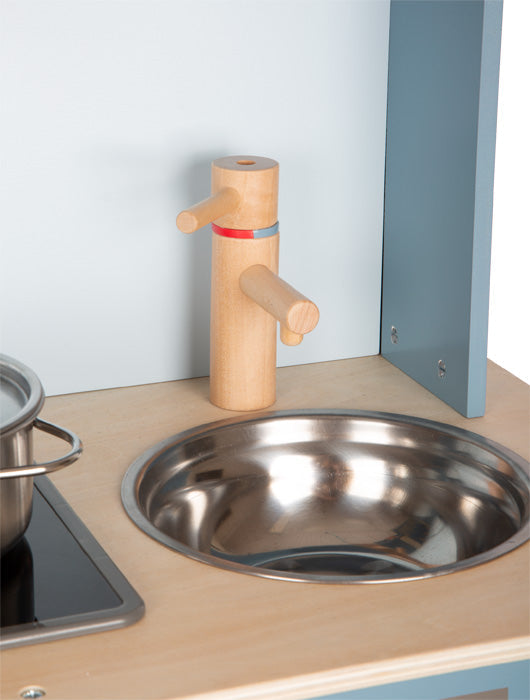 Spielküche als Designobjekt: Rauchblaues Spülbecken mit Holzarmatur und Metallschüssel neben Herdplatte mit Metalltopf.