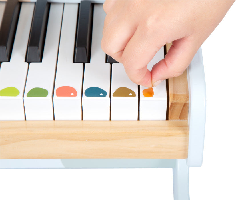 Eine Hand drückt eine weiße Klaviertaste mit kindgerechtem Motiv – einem farbigen Punkt – auf einem kleinen elektronischen Holzklavier, perfekt für musikalische Früherziehung.