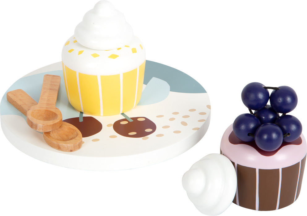 Zwei hölzerne Spielzeug-Cupcakes mit Teller, zwei Holzlöffeln und ein Cupcake mit lila Beeren – perfekt für die Kinderküche oder als stilvolles Kaffee- und Teeservice im skandinavischen Design.