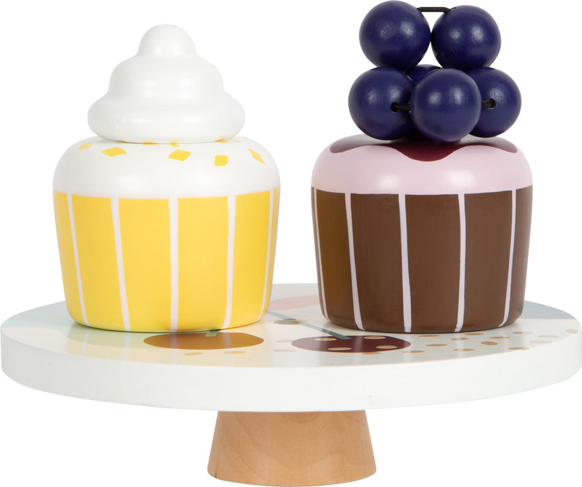 Zwei Spielzeug-Cupcakes – ein gelber mit weißem Zuckerguss und ein brauner mit violetten Beeren – stehen auf einem Holzständer, perfekt für jede Kinderküche oder als Akzent für Ihr Kaffee- und Teeservice im skandinavischen Design.