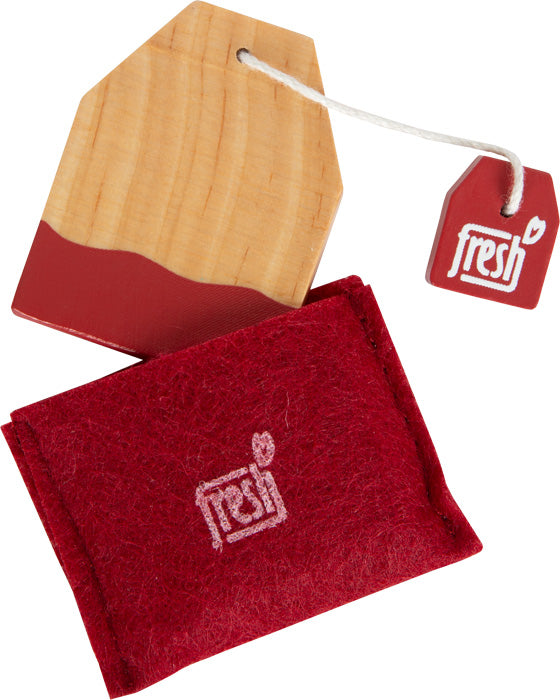 Ein hölzernes Objekt in Form eines Teebeutels und ein roter Filzbeutel, beide mit der Aufschrift „Fresh“ versehen, verleihen jedem Kinderküchen- oder Kaffee- und Teeservice-Spielset einen Hauch skandinavischen Designs.
