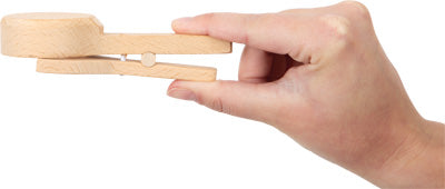Eine Hand hält eine große Wäscheklammer aus Holz und klemmt sie zwischen Daumen und Fingern – als würde man in der Kinderküche einen magnetischen Eisportionierer aus einem Eiscreme-Spielset greifen.