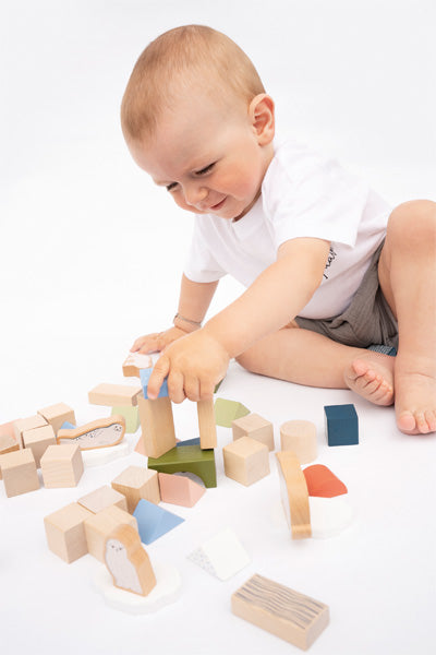 Ein Baby spielt mit einem Holzbaustein-Set, während es lächelnd auf dem Boden sitzt und Holzbausteine stapelt – ein spannendes motorisches Spielzeug für die frühe Entwicklung von Fähigkeiten.