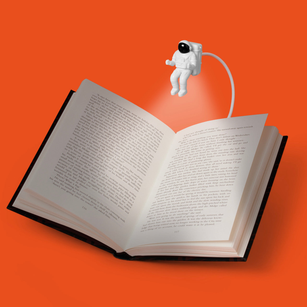 Ein offenes Buch wird von einer winzigen Astronaut-Leseleuchte beleuchtet, die vor einem leuchtend orangefarbenen Hintergrund einen LED-Lichtstrahl auf die Seiten wirft.