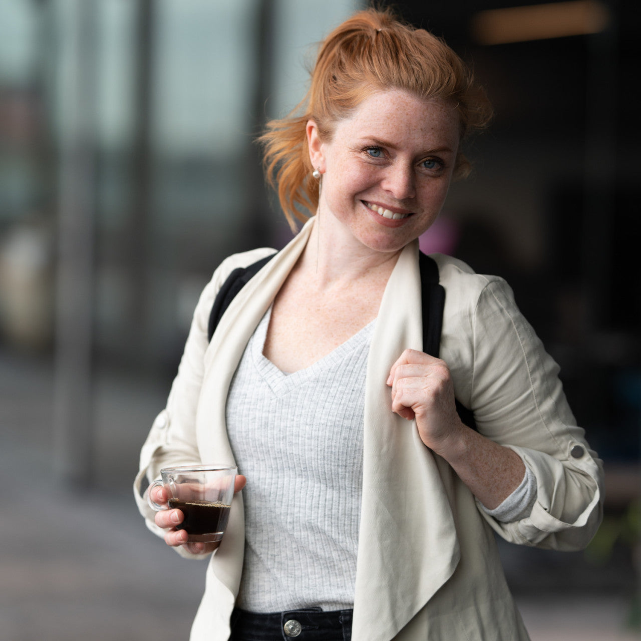 Lächelnde Frau mit roten Haaren hält ein Getränk und eine Tasche, steht im lässigen Outfit draußen und strahlt dank ihrer Flexi-Haltestütze Selbstvertrauen mit einer tollen Haltung aus.