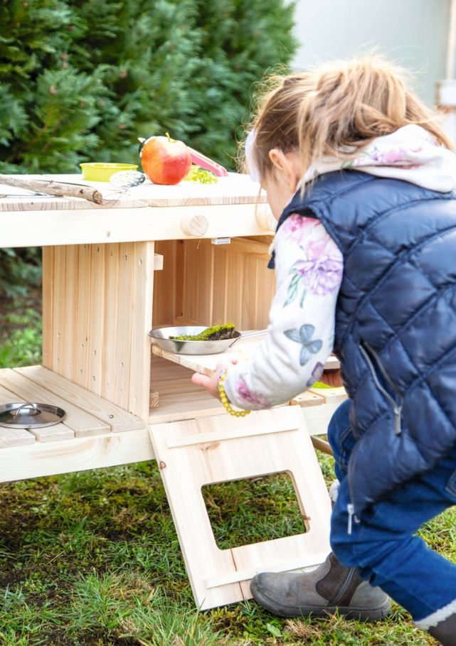 Mädchen, das in einer Matschküche für Kinder spielt und eine Metallschüssel hält.