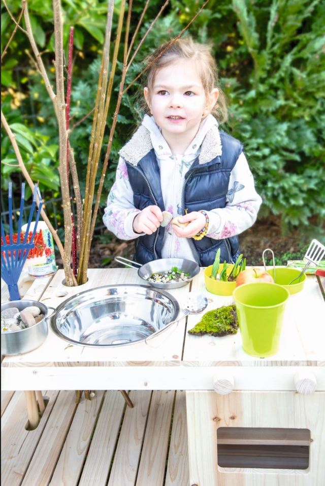Ein junges Mädchen spielt mit einer Matschküche für Kinder mit Spielzeugutensilien und -schüsseln.