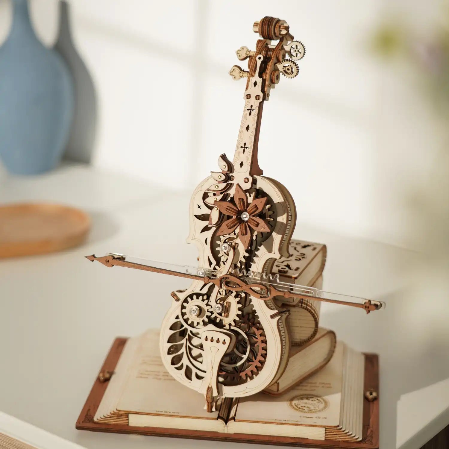 Das 3D Holzpuzzle „Magisches Cello“ ist ein mechanisches Holzmodell in Form einer Geige mit filigranen Zahnrädern und floralen Mustern. Es steht mit seinem Bogen auf zwei gestapelten Büchern und wirft im Sonnenlicht einen sanften Schatten – ein ideales Stück für jeden Musikliebhaber.