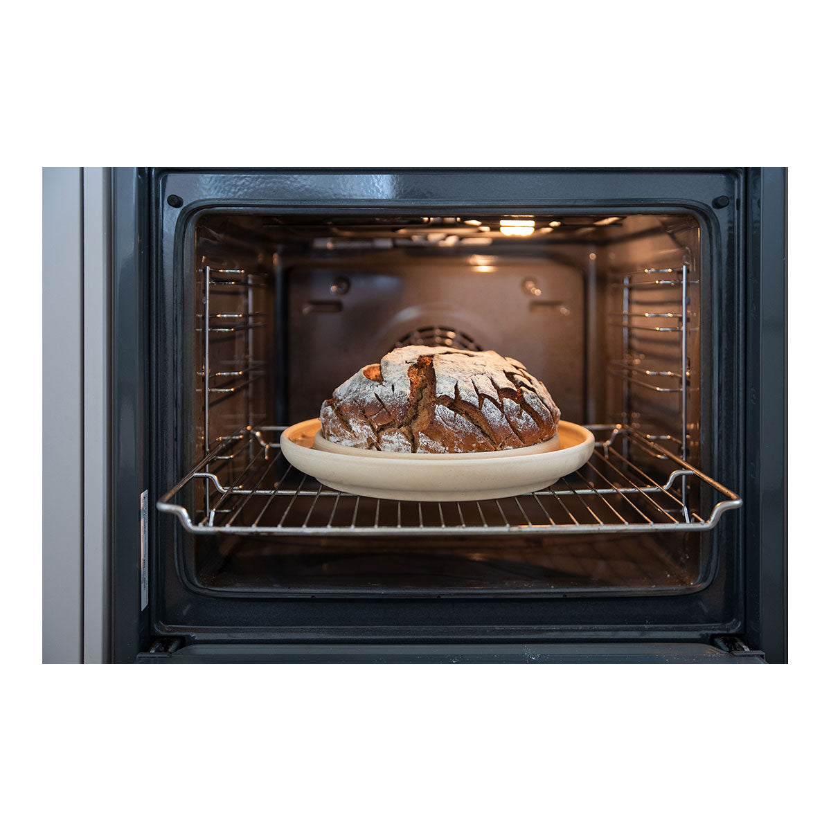 Ein frisch gebackenes rustikales Brot liegt auf einem runden Teller im offenen Backofen.