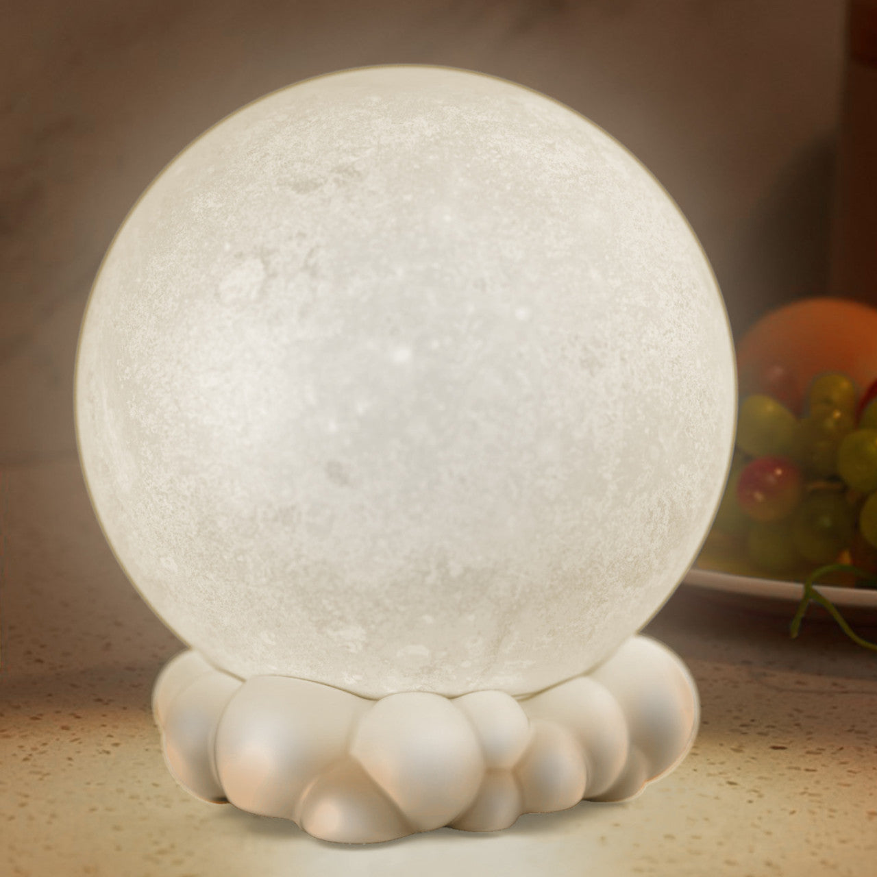Ein leuchtendes, 3D-gedrucktes, mondförmiges Nachtlicht sitzt auf einer wolkenähnlichen Basis, mit Trauben und einer Orange im Hintergrund.