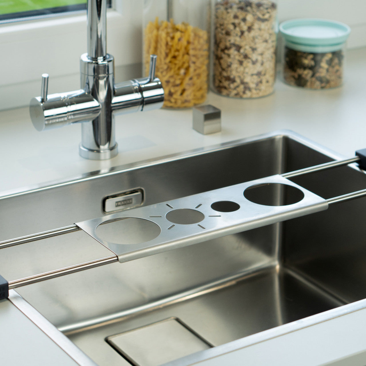 Der Nudelsiebeinsatz aus Metall und Edelstahl mit mehreren Lochgrößen dient als praktische Abtropfstation und wird über einer Küchenspüle in der Nähe des Wasserhahns und der Lebensmittelgläser platziert.