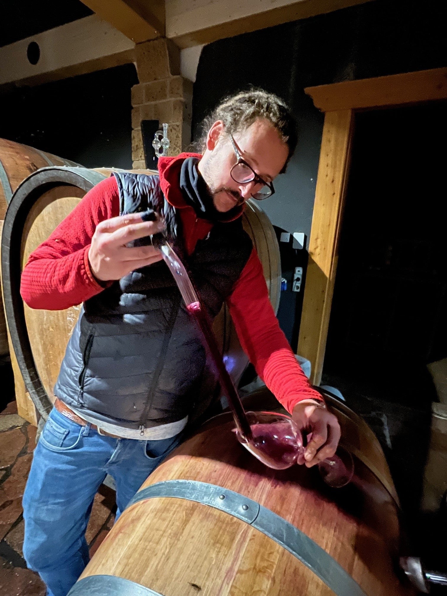 Eine Person lässt sich in einem schwach beleuchteten Keller mithilfe eines Weindiebs den Stuttgarter Zeitung Weinedition 2024 Lemberger + Chardonnay aus einem Fass verkosten.