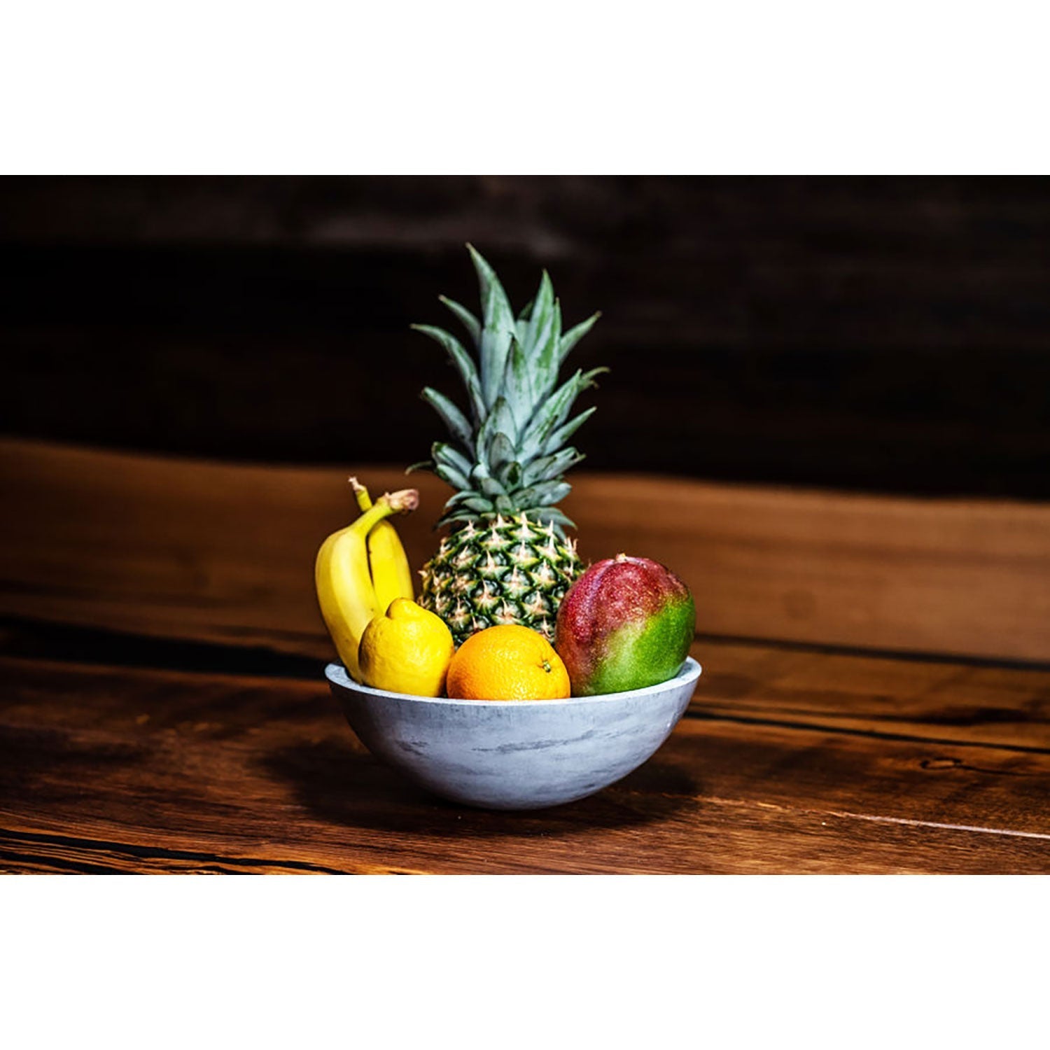 Runde Betonschale gefüllt mit Ananas, Bananen, Mango und Zitrone auf Holztisch