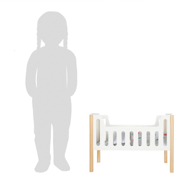Eine Kindersilhouette steht neben einem weißen Puppengitterbett mit Holzbeinen zum Größenvergleich und unterstreicht so sein skandinavisches Design.