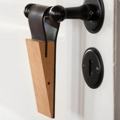 Der hölzerne Türstopper STOPPERMAUS in Mäuschenform hängt an einem schwarzen Griff in der Nähe des Schlüssellochs einer weißen Tür und verleiht als Design-Türstopper Charme und Funktionalität.