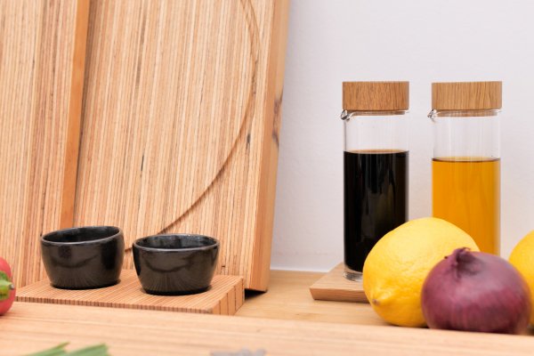 Zwei Soßenflaschen, zwei schwarze Tassen, Zitronen und eine Zwiebel ruhen auf einer Holztheke mit Schneidebrettern aus heimischer Buche. Designerin Annegret Ewert-Wurster bringt Eleganz in den Küchenalltag.