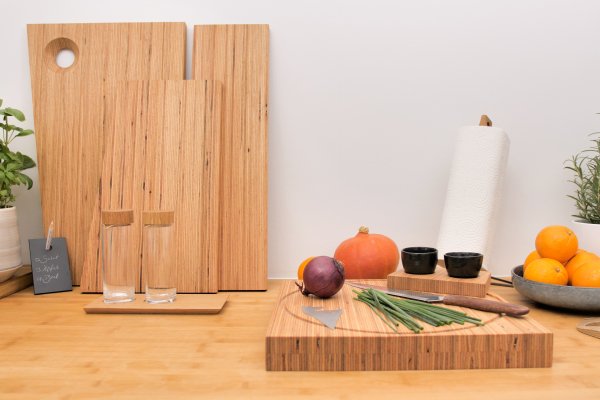 Eine moderne Küchenarbeitsplatte mit Schneidebrettern aus heimischer Buche, Gewürzen, Gemüse, Kräutern und einem Messer auf einem von Annegret Ewert-Wurster entworfenen Furnierschichtholz-Schneidebrett.