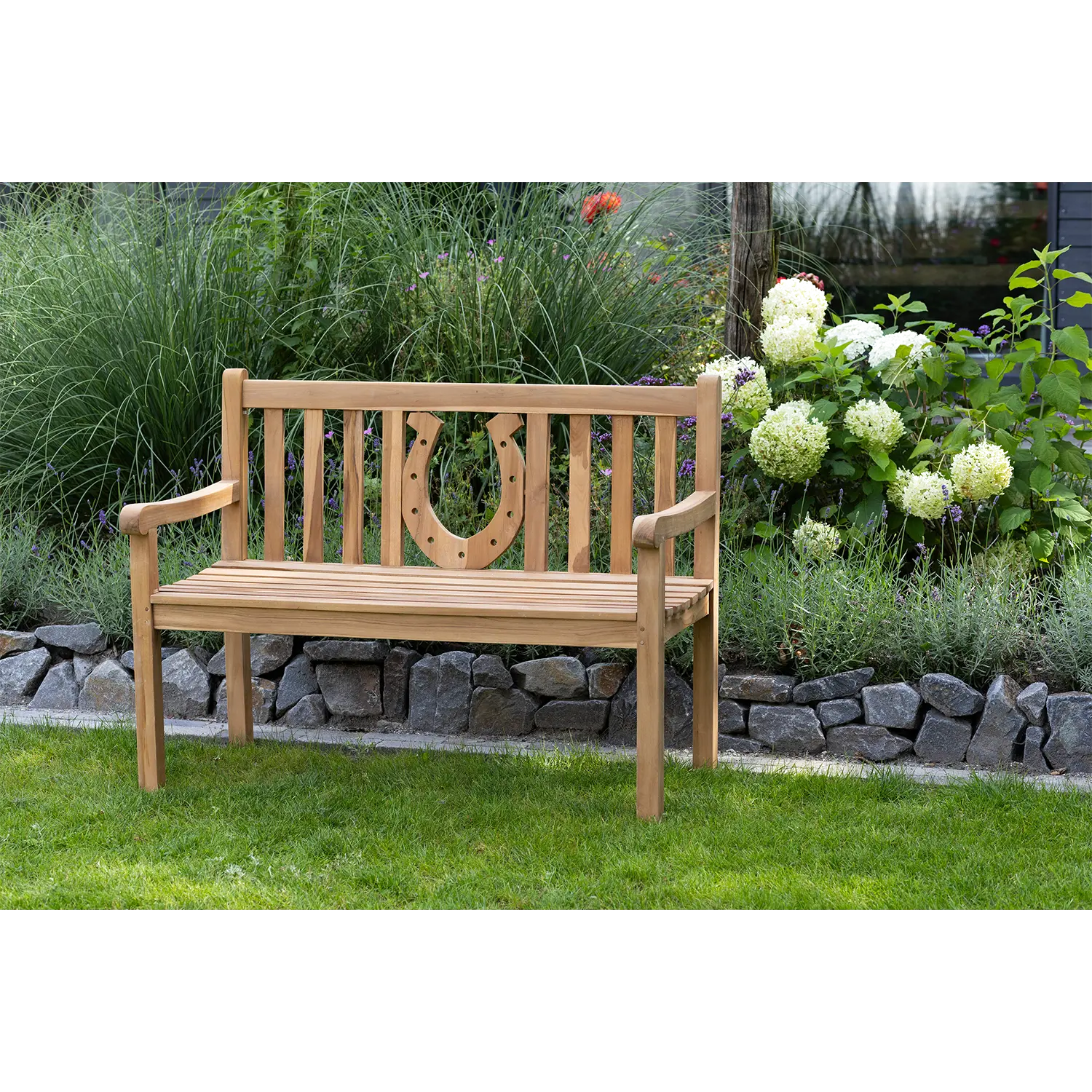 Gartenbank aus Teak mit Hufeisen-Motiv steht auf Gras bei Blumen.