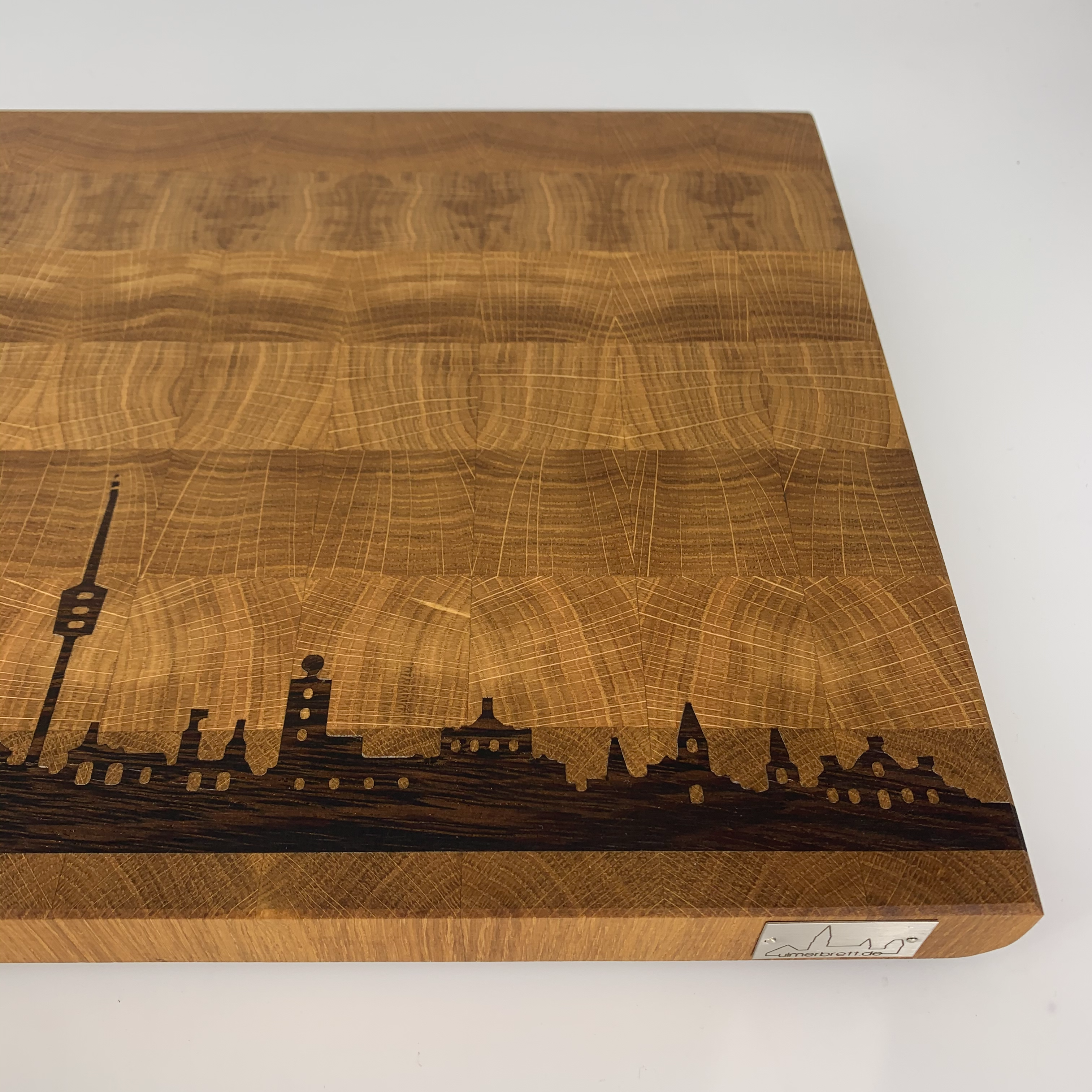 Stirnholz-Schneidebrett aus Holz mit einer dunkel eingravierten Skyline einer Stadt entlang einer Kante vor einem weißen Hintergrund, ein Ausdruck exquisiter Handwerkskunst.