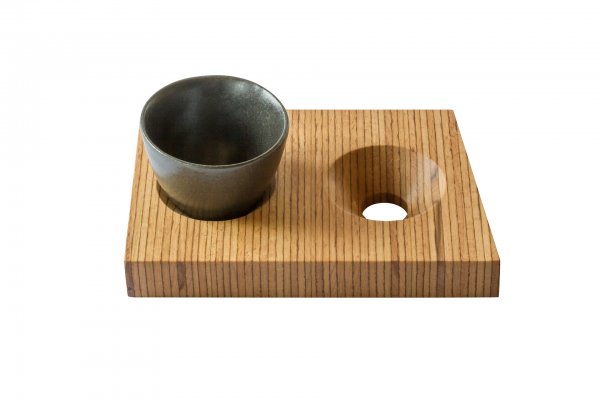 Eine kleine Keramiktasse sitzt auf einem Holzblock aus heimischer Buche mit zwei kreisrunden Vertiefungen, von denen eine die Tasse hält – eine Kreation der Designerin Annegret Ewert-Wurster.