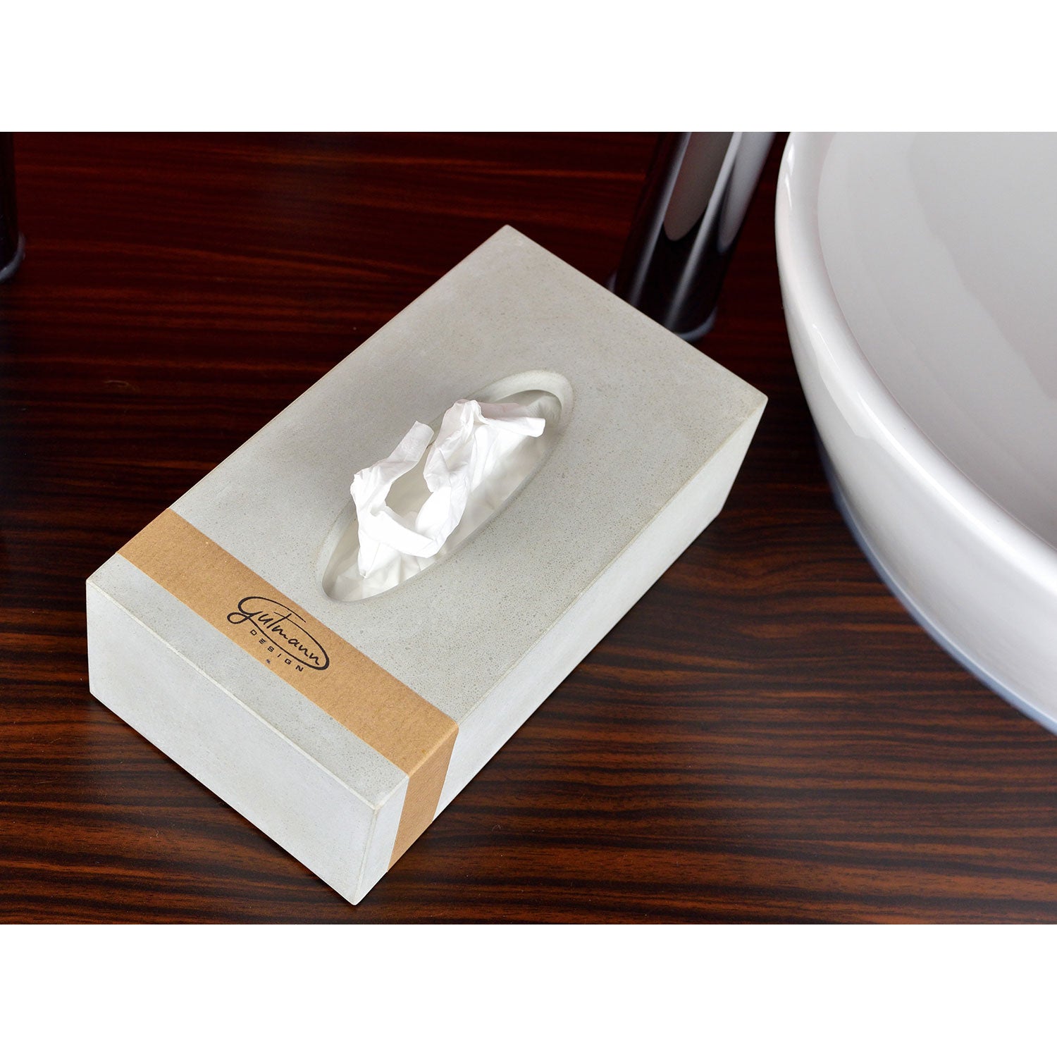 Die „Taschentücherbox aus Beton“ in Betonoptik mit beiger Hülle, die den Markennamen präsentiert, steht auf einer dunklen Holzoberfläche neben einer weißen Schale, aus der oben ein zerknülltes Taschentuch ragt und fängt moderne Ästhetik ein.