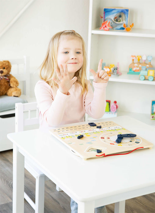 Ein junges Mädchen sitzt an einem Tisch und zählt mit den Fingern. Vor ihr steht eine Lernuhr von Holzspielzeug, die dabei hilft, die Feinmotorik zu entwickeln.