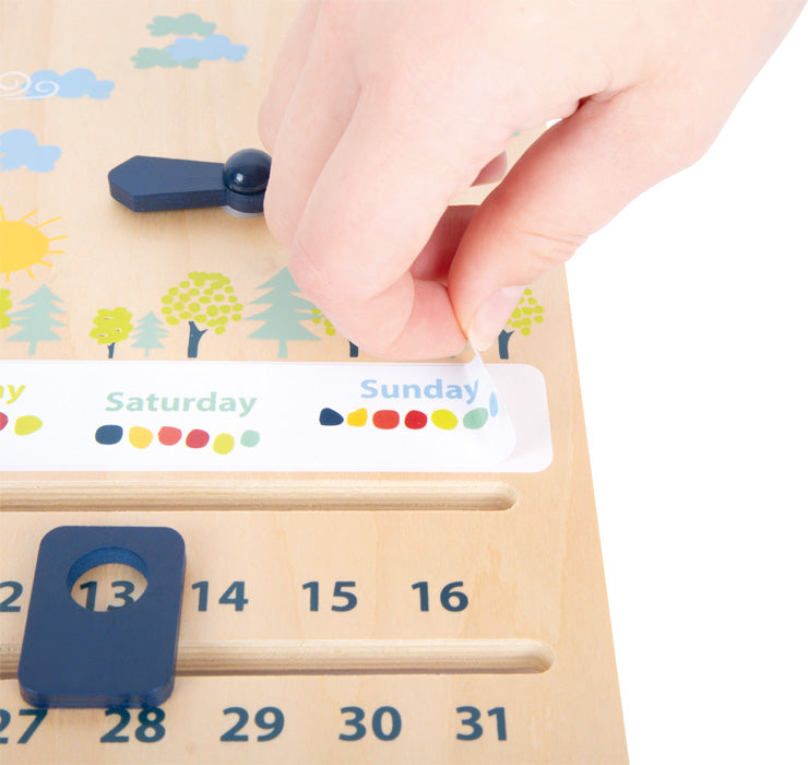 Eine Hand stellt einen hölzernen Kalender mit beweglichen Teilen für Tage und Daten ein, ein bezauberndes Holzspielzeug, das hilft, die Feinmotorik zu entwickeln.