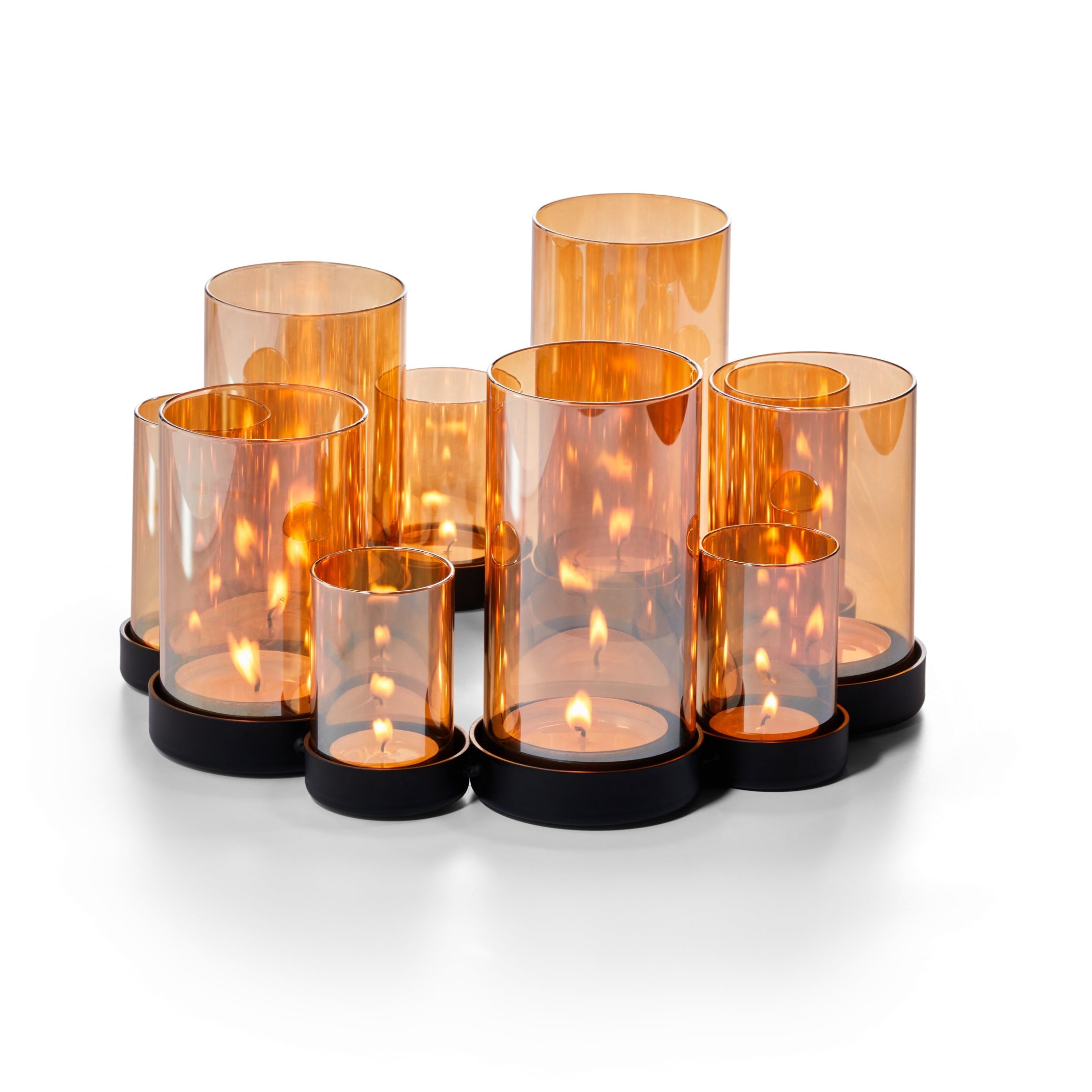 Eine Gruppe orangefarbener Kerzenhalter aus Glas mit brennenden Kerzen auf einem schwarzen Tablett, in verschiedenen Höhen angeordnet, erzeugt ein warmes Lichtspiel über die verspiegelten Glasröhren.