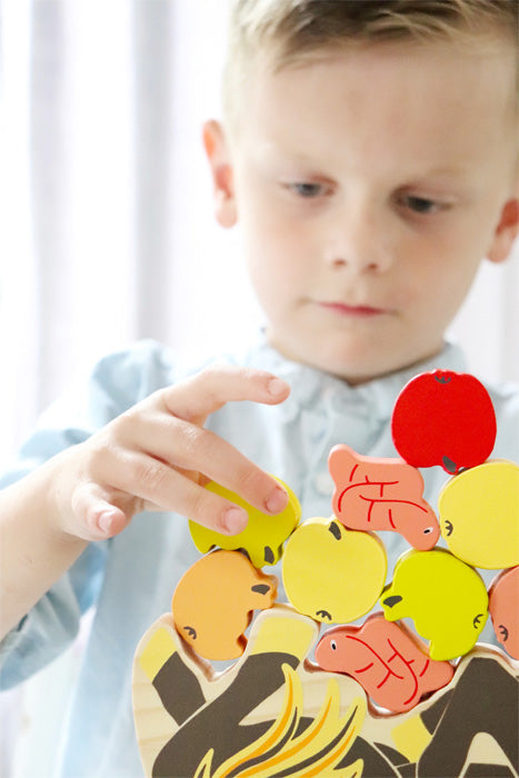 Ein kleiner Junge stapelt bunte Obststücke aus Holz