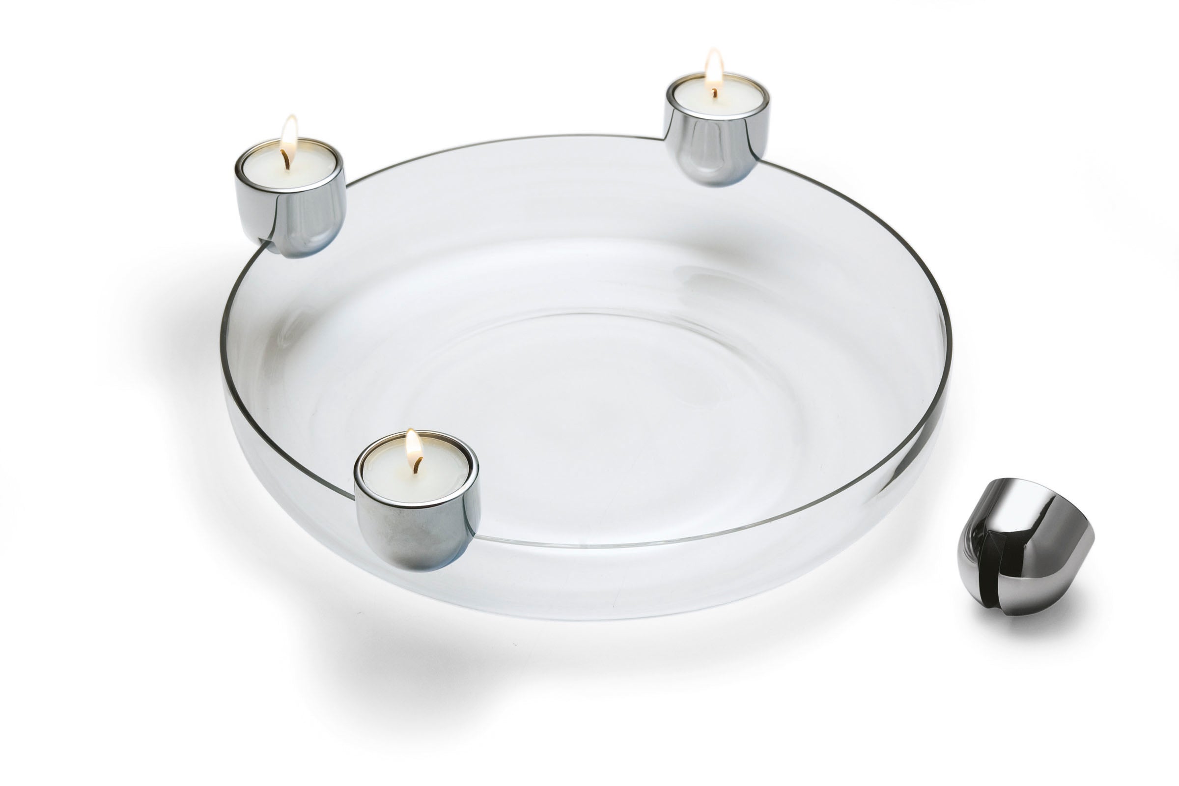 Auf einem Glasteller befinden sich drei ARENA Teelichthalter aus Metall mit brennenden Teelichtern, daneben steht ein vierter Kerzenhalter, der für eine moderne Note sorgt, die an einen Adventskranz erinnert.