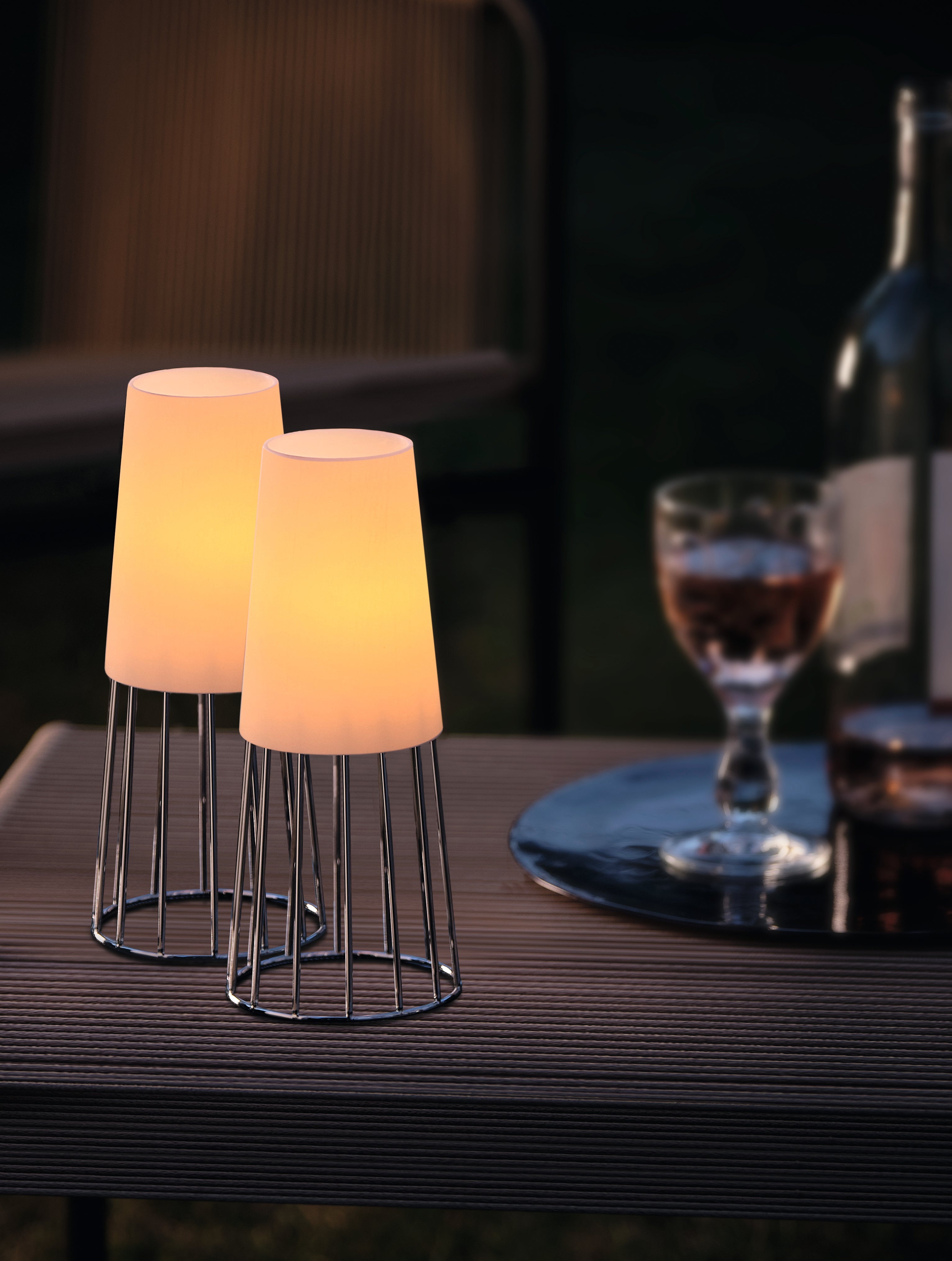 Zwei moderne Tischlampen mit zeitlosem Design leuchten auf einem Holztisch neben einem Glas Roséwein, einer Weinflasche und einem Teelichter-Set – perfekt als elegantes Geschenk.