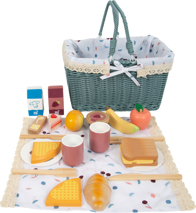 Ein Picknick-Spielset mit einem Picknickkorb, Spielzeuglebensmitteln, Tassen, Tellern und Besteck, ordentlich angeordnet auf einer gemusterten Picknickdecke.