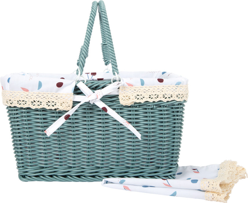 Grüner Picknickkorb aus Weide mit Spitzenbesatz, einem weißen Stofffutter und einer passenden gefalteten Picknickdecke daneben – perfekt für stilvolle Zusammenkünfte im Freien.