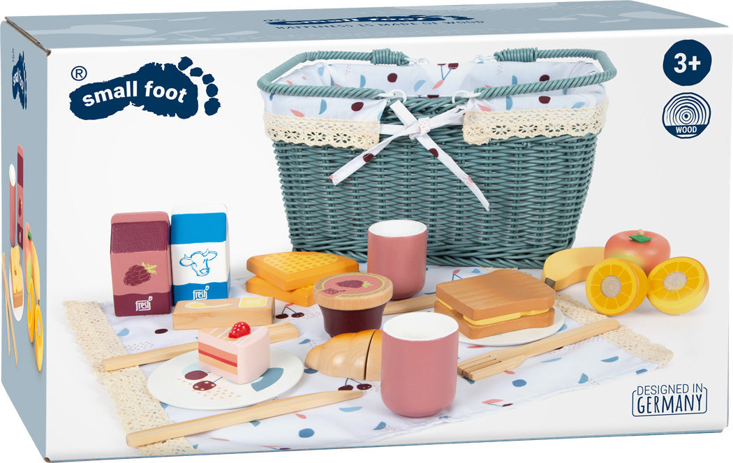 Spielzeug-Picknickset mit Lebensmitteln, Getränken und einem grünen Picknickkorb aus Holz auf einer gepunkteten Picknickdecke; perfektes Spielset für Kinder ab 3 Jahren.