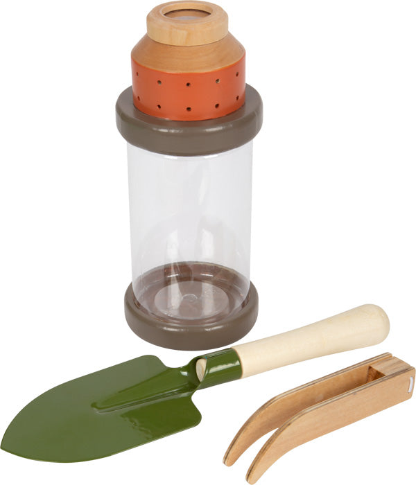 Ein Insektenbeobachtungsglas mit einer grünen Schaufel und einer Holzpinzette daneben – ideales Entdeckerspielzeug für junge Forscher, das sie auf spannenden Abenteuertouren in ihren Rucksack packen können.