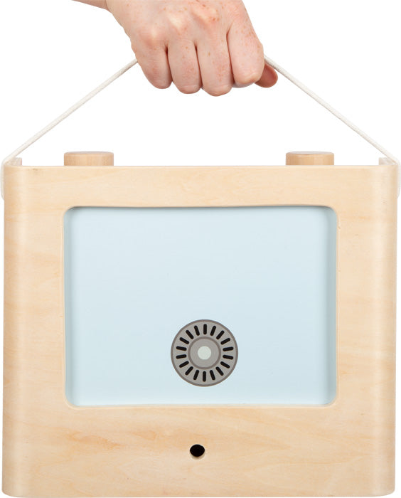 Eine Hand hält einen Campingkoffer – eine multifunktionale Spielküche in Form einer Kinder-Küche, mit Holzgriff, blauem Frontpanel und rundem Lüftungsschlitz in der Mitte.