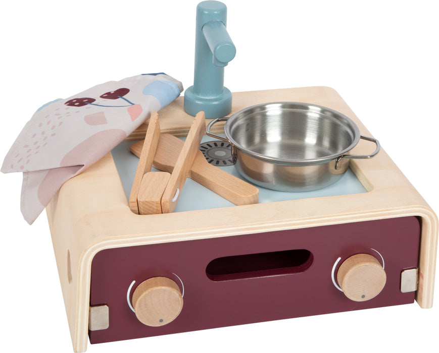 Multifunktionale Spielküche aus Holz mit Spüle, Wasserhahn, Metalltopf, Utensilien und Tuch auf einer hellen Oberfläche – perfekt für kleine Köche.