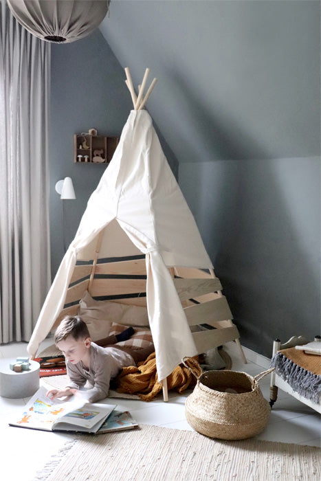 Kleines Kind liest in einem Outdoor Zelt Tipi für Kinder in einem gemütlichen Kinderzimmer.