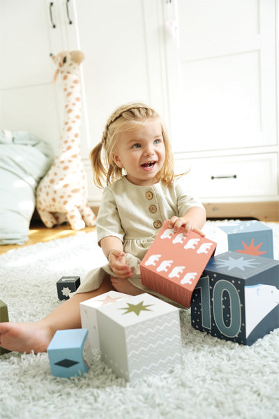 Lächelndes Kleinkind, das mit bunten Stapelwürfeln auf einem weißen Teppich spielt, mit einer Plüschgiraffe im Hintergrund – die Fantasie verwandelt die Spielzeit in eine arktische Landschaft voller freundlicher Polartiere.