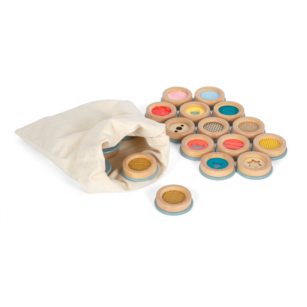 Ein Stoffbeutel mit ausgebreiteten hölzernen Sensorikscheiben aus der Sinnesspiel Sensory Produktlinie, jede mit unterschiedlicher Textur und Farbe.