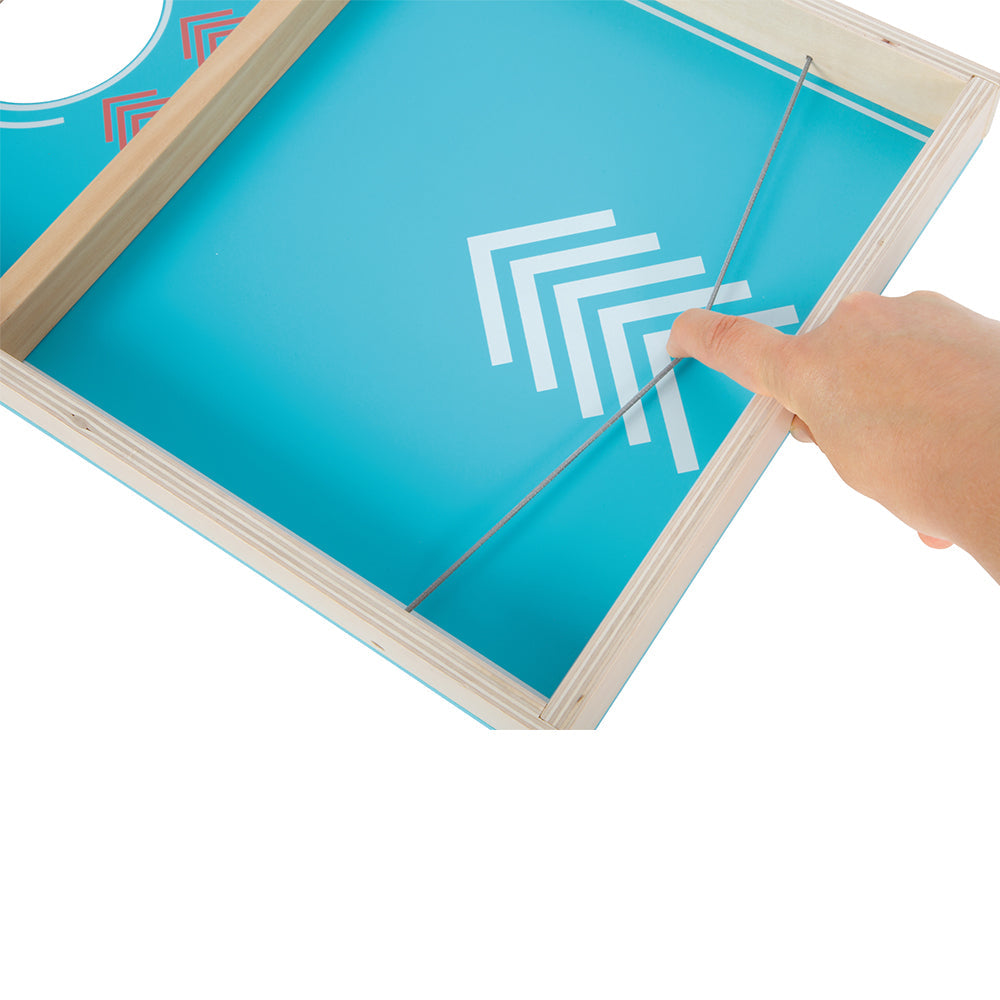 Eine Hand zieht ein Gummiband auf einem blauen Sling-Puck-Spielbrett aus Holz zurück, das mit weißen geometrischen Mustern verziert ist.