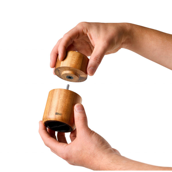Zwei Hände trennen vor weißem Hintergrund den oberen und unteren Teil einer Seedo-Gewürzmühle mit PolyCut-Mahlwerk, einem zylindrischen Holzobjekt, das sich ideal zum Mahlen ölhaltiger Saaten eignet.