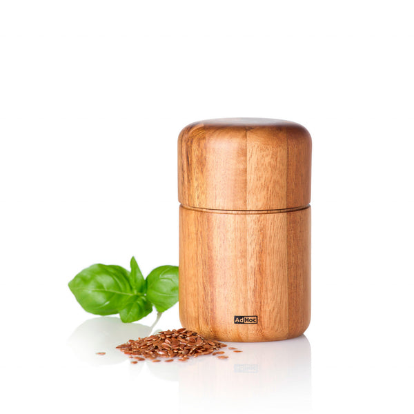 Hölzerne Gewürzmühle von Seedo mit Leinsamen und Basilikumblättern daneben auf weißem Hintergrund, ausgestattet mit einem PolyCut-Mahlwerk zum perfekten Mahlen ölhaltiger Saaten.