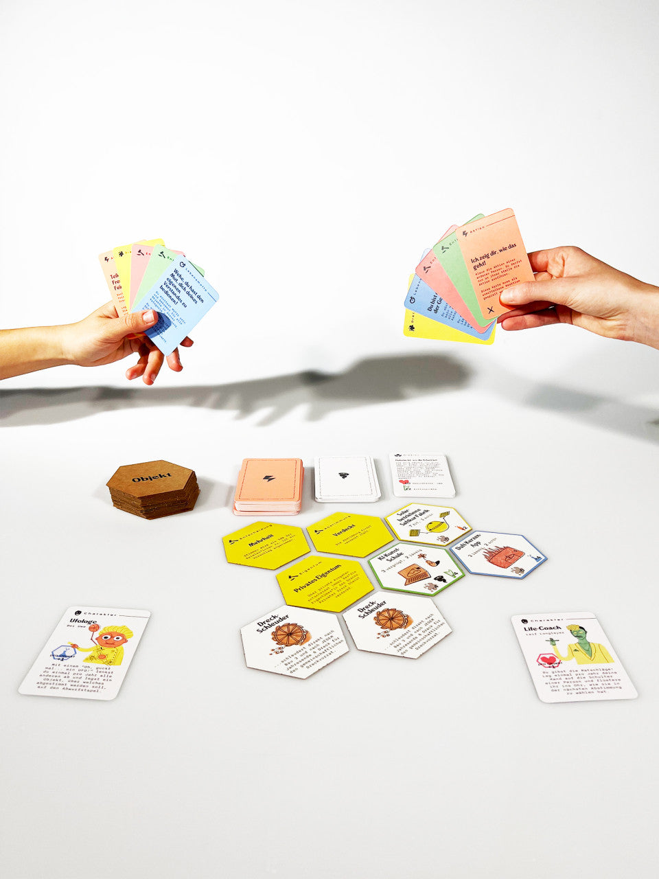 Zwei Personen halten bunte Karten in der Hand, während sie auf einer weißen Fläche ein Gesellschaftsspiel für Weltraumreisende spielen und dabei die Geheimnisse eines verlassenen Planeten erkunden.