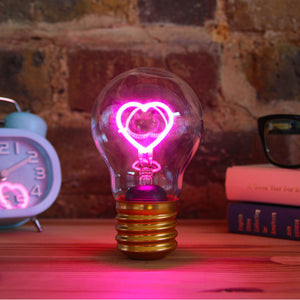 Ein leuchtender rosa Glühfaden in Herzform in einer Edison-Glühbirne, mit Büchern und einer Uhr im Hintergrund.