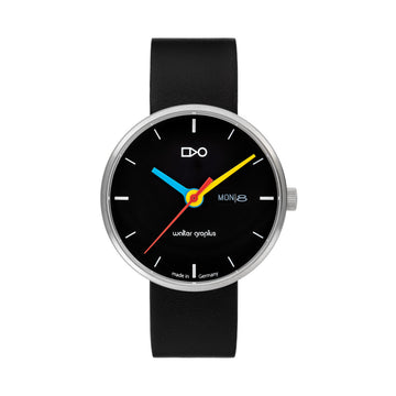 Eine minimalistische schwarze Armbanduhr mit bunten Zeigern und einem schwarzen Lederarmband, die Tag und Datum im echten Bauhaus-Stil anzeigt.