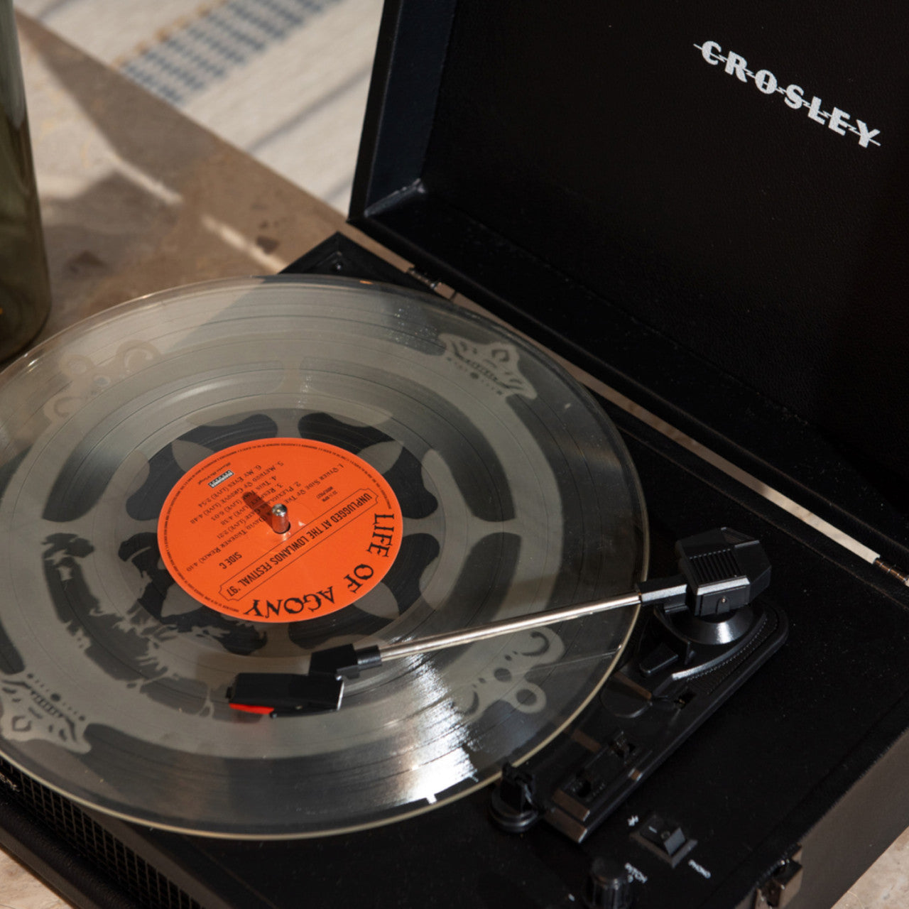 Eine klare Vinyl-Schallplatte wird auf einem schwarzen Crosley Bluetooth Voyager-Plattenspieler unter natürlichem Licht abgespielt.